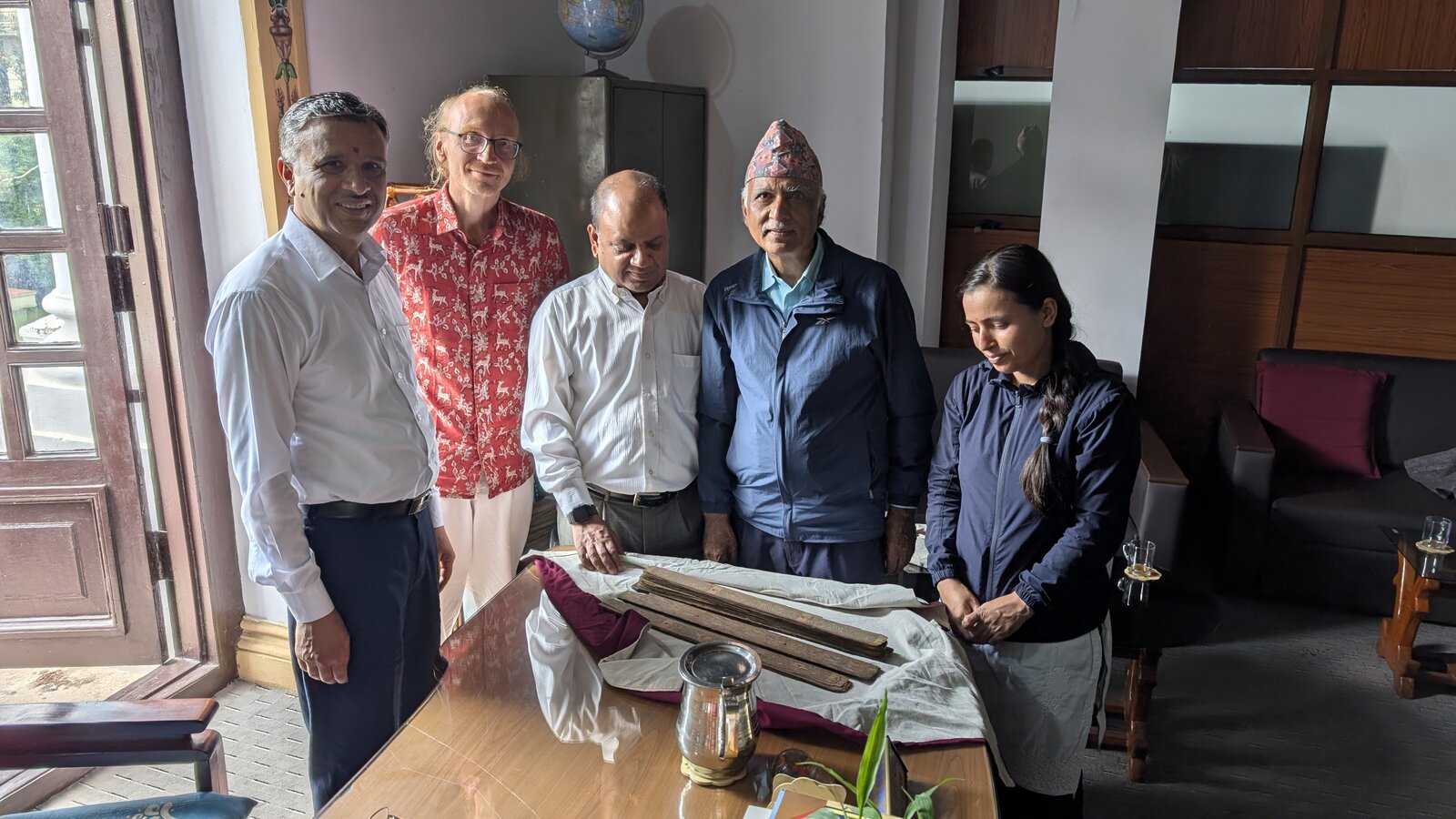 Five people standing around a table on which the palm leaves of MS KL 699 lie on their wrapping cloths