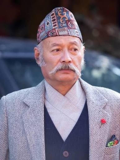Portrait of Madhu Bajra Bajracharya wearing a patterned Nepali dhaka topi and a grey tweed jacket