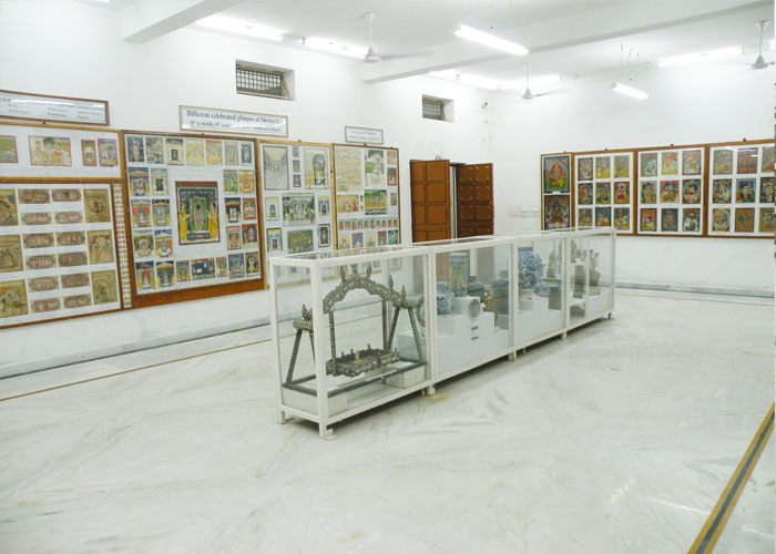 A gallery hung with paintings, with porcelain and a silver swing in a central display case